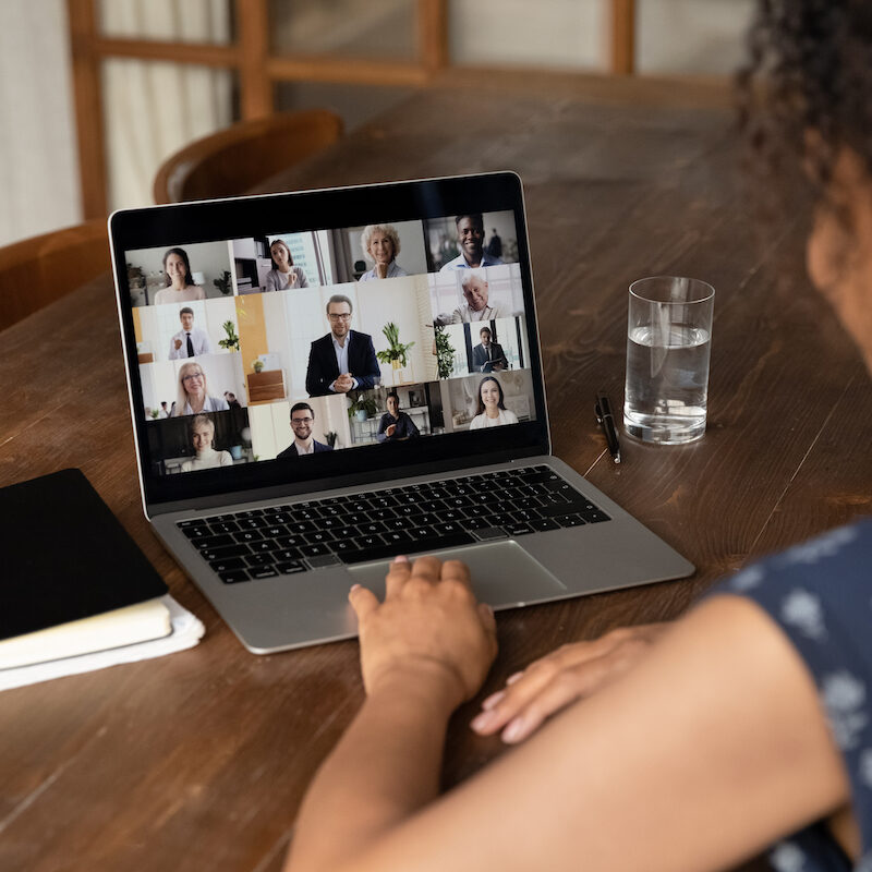 Rear view of female employee talk online video call with diverse multiracial colleagues at home office. Woman worker have webcam digital virtual conference or web meeting with businesspeople.