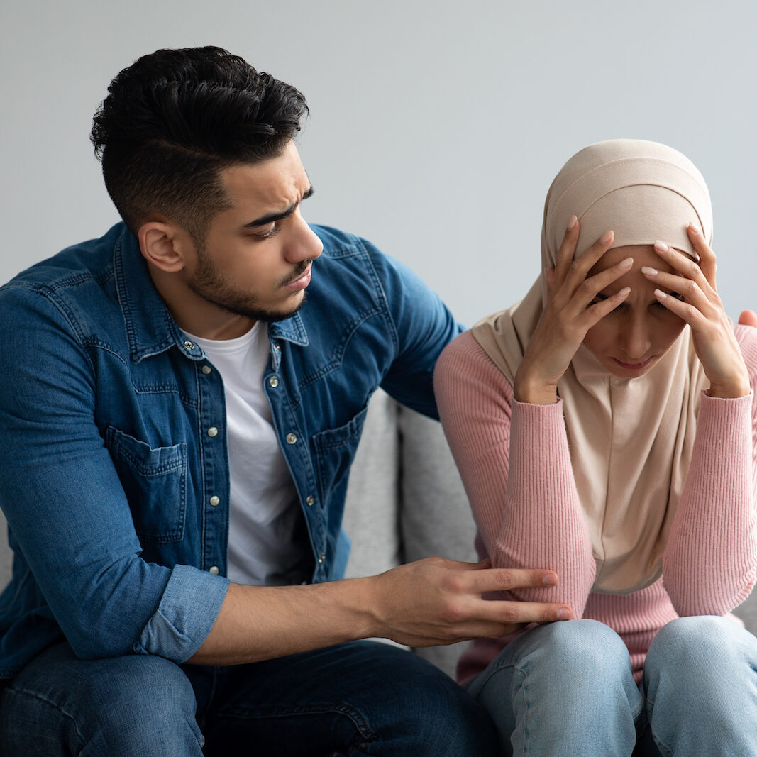 Middle-eastern bearded man comforting his crying wife, young muslim couple having problems in relationships, visiting family therapist together. Frustrated lady in hijab feeling unhappy