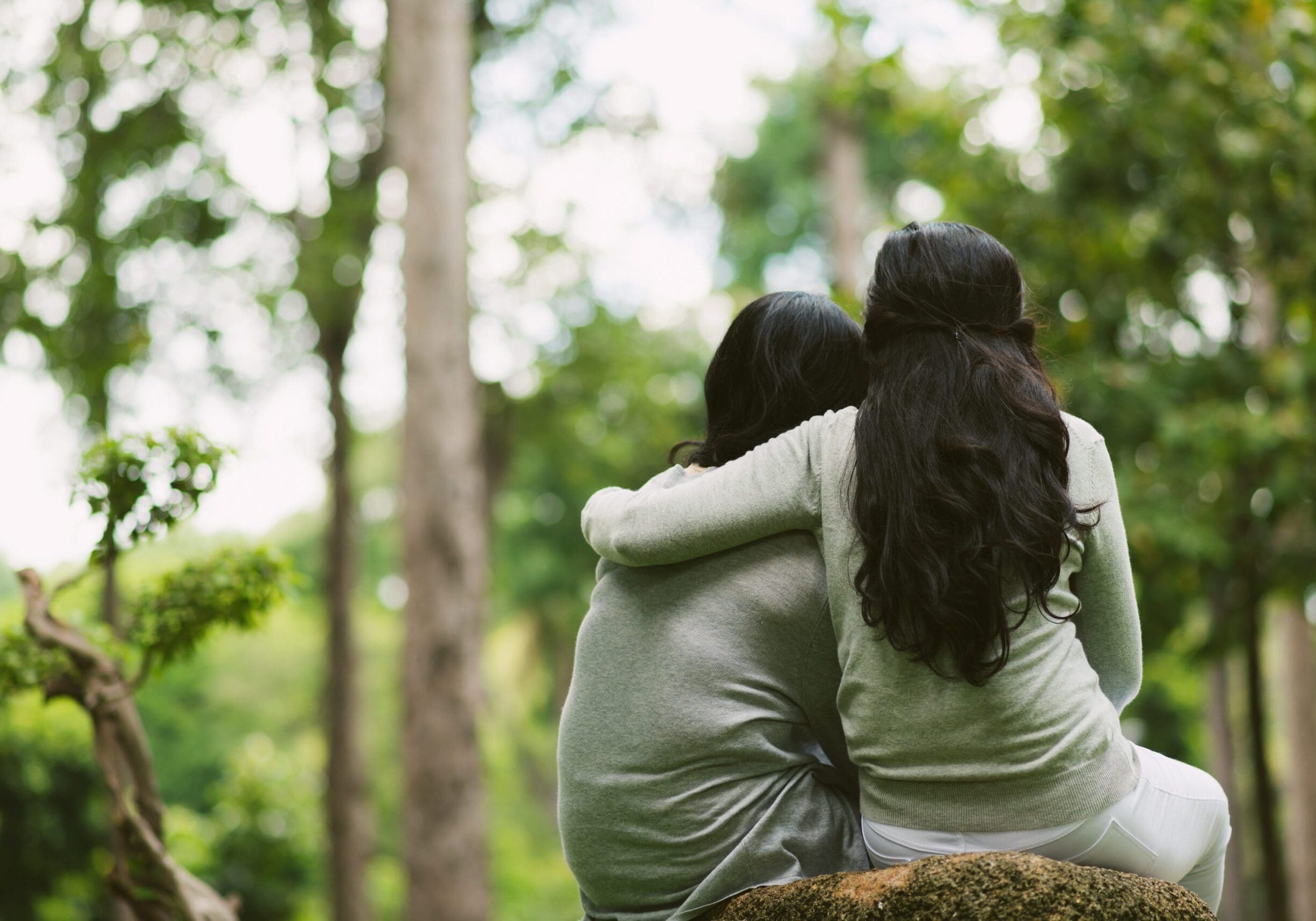 Vista trasera de amigas abrazándose sentadas en el parque